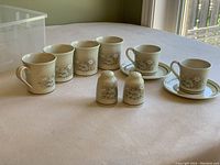 Tea and coffee set with two teacups and saucers, four coffee mugs, and salt and pepper shakers arranged on table.