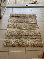 Full view of the rectangular shaggy carpet with cream and brown horizontal stripes placed on a tiled floor.