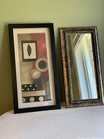 Two wall decor items displayed side by side: an MCM abstract print in black frame and a gold and black framed rectangular mirror.
