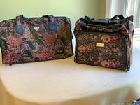 Two floral patterned bags, one duffle and one tote, displayed on a surface near window light.