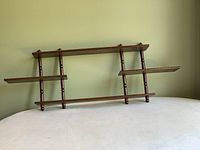 Full view of the wooden wall shelf showing three shelves and spindle supports in medium brown finish.