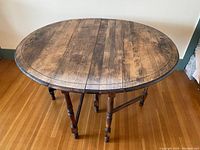Top view of oval oak drop leaf table showing wood grain and carved decorative detailing near edges.
