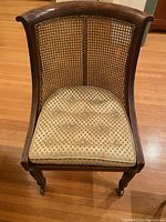 View of chair from front showing curved wooden top and cane backrest with upholstered tufted seat.