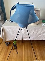 Blue mesh lampshade on black tripod base desk lamp shown from side angle with cord visible on the floor.