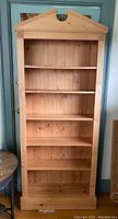 Front view of tall maple bookshelf showing six shelves and decorative pediment