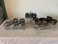 Photo showing three groups of vintage glassware with silver fade rims and floral etching arranged on metal carrier trays on a beige cloth.