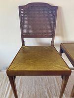 Front view of one folding chair showing cane back with wooden frame and olive vinyl seat.