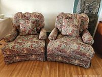 Front view of two large lounge armchairs with colorful safari animal print upholstery showing the full chairs and matching pillows on hardwood floor.
