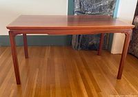 Front view of the rectangular teak coffee table showing smooth top, tapered legs and carved apron detail.