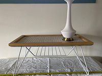 Side and angled views showing the rectangular vintage table with cream tiled top, wooden frame, white hairpin legs, and wire magazine rack underneath.