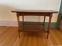 Front view of vintage walnut side table showing straight legs and lower shelf.