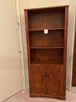 Front view of a medium brown wooden bookcase with three shelves and lower cabinet doors closed.