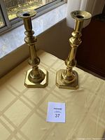Pair of heavy brass candlesticks on a table with natural light, showing general design and size relation