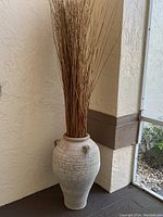 Full view of large terra cotta vase filled with tall decorative reeds placed in a corner.