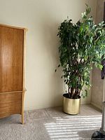7-foot artificial Ficus tree in a gold-colored pot placed next to a wooden cabinet, showing the full size and appearance.