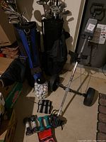 Full view of two sets of golf clubs in respective bags, jar of golf balls, push cart, ankle and hand weights, and metal dexterity balls on floor.