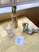 Front view of the two Lladro figurines and glass bud vase on a yellow checkered tablecloth