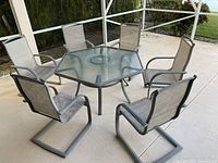 Full view of the hexagonal outdoor patio table surrounded by six sling chairs on patio surface.