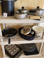 Full view of all cookware and baking items on two shelves including pots with lids, baking racks, colander, and pans.