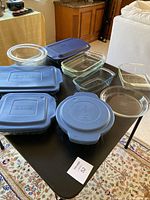 View of glass serving dishes with blue Anchor plastic covers on a table.