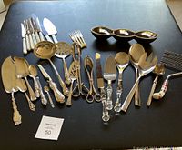 Top down view of entire set of sterling and silver plate serving pieces arranged on black table surface.