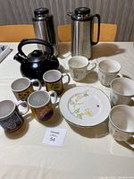 Overview of all items: four decorative ceramic coffee mugs, four white floral teacups and saucers, black tea kettle, and two stainless steel insulated coffee pitchers.