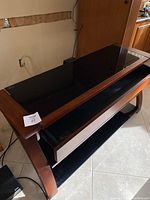 Top view of tempered black glass TV stand showing cherry wood trim and drawer beneath the top shelf.
