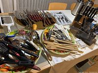 Overview photo showing the entire collection of cutlery, knives, wooden utensils, and kitchen tools arranged on table.