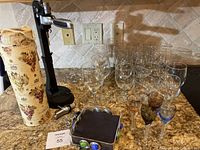 Full display of tall and short wine glasses, colored aperitif glasses, and wine accessories on granite countertop against a backsplash.