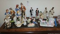 Full lot overview featuring diverse collectible figurines including Royal Doulton couples, nativity figures, Asian figurines, and Schmid music box stagecoach
