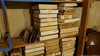 Stack of various original and empty boxes for collector plates on wooden shelves in a basement setting.