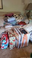 Full view of bed linens and quilts stacked on couch, packaged in bags, with scarf ring hanger on top