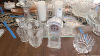 Wide view showing multiple crystal and cut glass items arranged on a wooden table including decanter, mantle clock, vases, crystal bowls, and candle holders with candles