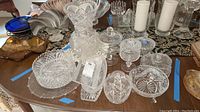 Overview photo showing various crystal and cut glass items arranged on a wooden table including bowls, vases, compotes, and candy dishes