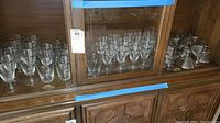 Wooden cabinet shelf displaying sets of clear Rosenthal crystal stemware including large and small glasses.