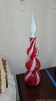 Full view of the Empoli decanter showing its tall slender stopper and red glass body with white spirals.