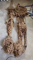 Two macrame hanging holders made of natural fiber rope laid on carpet showing detailed knot work, tassels, and wooden beads