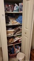 Open closet with multiple shelves holding assorted folded table linens including tablecloths, placemats, and napkins.