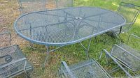 Full view of rectangular metal mesh patio table with six matching chairs on grass.