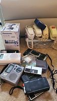 Lot of Panasonic cordless phones, vintage landline phones, and related accessories displayed on sofa with original packaging