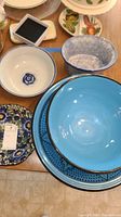 Table display of six artisan pottery bowls and plates including a large blue bowl, medium blue bowl, white bowl with blue rose, small oval speckled blue bowl, and floral plate