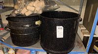 Two black enamel speckleware pots, one large stock pot with handles, one smaller pot with lid, and a plastic bag of wooden wine corks.