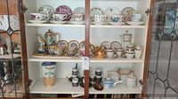 Cabinet of multiple tea sets, bowls, cups, and decorative items showing full variety of porcelain collections and ceramics