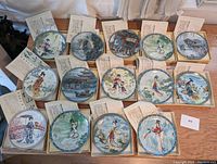 Front view of all 14 plates arranged in boxes showing decorative scenes