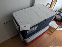 Blue Coleman chest cooler with gray lid and side handles, stacked on red Igloo chest cooler with white lid in indoor setting