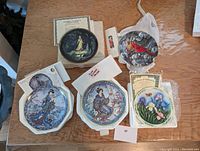 Top front view showing all five collector plates arranged with certificates and packaging material on a wooden surface.