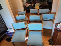 Eight dining chairs arranged in two rows, showing wooden frames and blue upholstery.