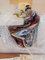 Close-up of porcelain sculpture partially wrapped in bubble wrap, showing painted details and gold accents.