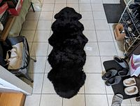 Full top view of the black Auckland sheepskin rug laid out on a tiled floor showing its length and natural shape.
