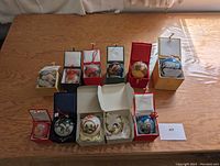 Full lot view showing 11 hand-painted glass Christmas ornaments displayed in individual presentation boxes on a wooden surface.